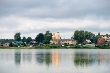 Fototapeta na wymiar View of the Trinity Church and residential buildings on Kirov street across Lake Bologoe. City Bologoe, Tver region, Russia