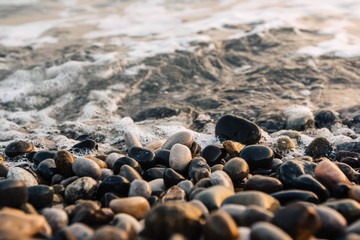 Small stones by the sea with bokeh effect. Blurred decorative background, place for text. Summer wallpaper, sunny sunset light
