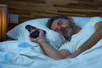 night portrait of young stressed and paranoid American man in bed sleeping and holding gun fearing...