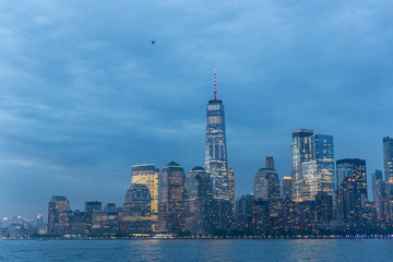 Panoramic view of Lower Manhattan from Ellis Island at cloudy dusk, New York City.