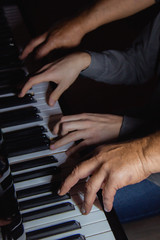 Fototapeta na wymiar playing four male hands on the piano. palms lie on the keys and play the keyboard instrument in a music school. student learns to play. hands of a pianist. black dark background.