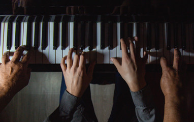 playing four male hands on the piano. palms lie on the keys and play the keyboard instrument in a...
