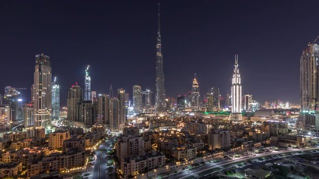 Dubai Downtown skyline all night timelapse with Burj Khalifa and other towers paniramic view from the top in Dubai, United Arab Emirates. Lights swithcing off. Traffic on circle road and fountains.