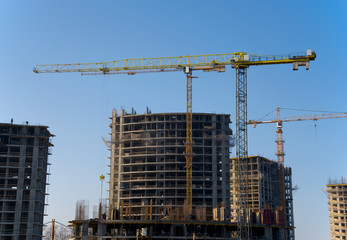 Tower cranes constructing a new residential building at a construction site against blue sky. Renovation program, development, concept of the buildings industry.