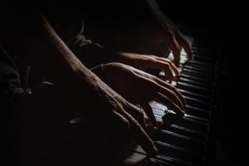 Fototapeta na wymiar playing four male hands on the piano. palms lie on the keys and play the keyboard instrument in a music school. student learns to play. hands of a pianist. black dark background.