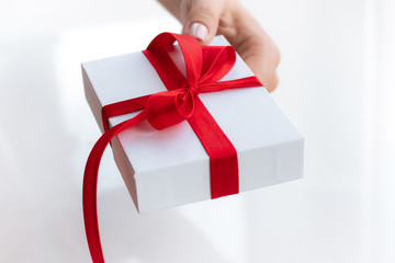 Gift present box with a red ribbon bow isolated on a bright white background. Passing present for a valentine's day from hand to hands. Love and holiday concept.