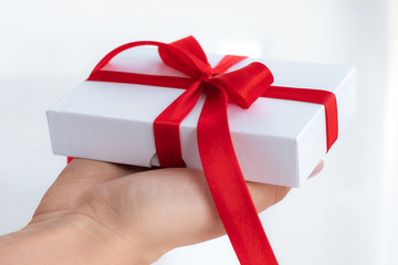 Gift present box with a red ribbon bow isolated on a bright white background. Passing present for a valentine's day from hand to hands. Love and holiday concept.