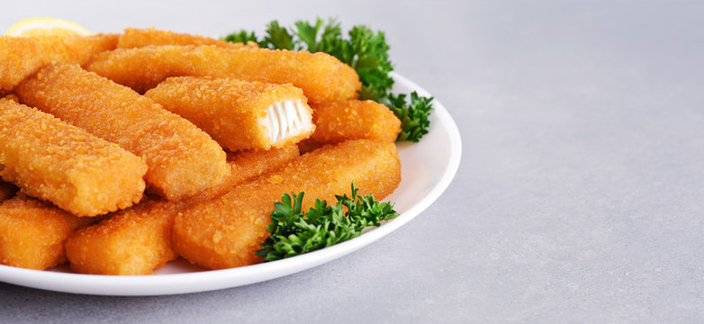 Fish fingers sticks on a plate with parsley and lemon on a gray texture.