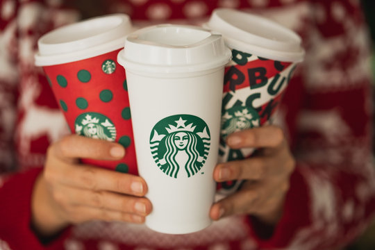 New York, USA - December 4, 2019: Close Up of a Woman wearing a Christmas Sweater Holding Three Tall Starbucks Cup. One Original Cup and Two Designing for 2019 Christmas Holiday.