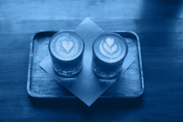 Two glasses of cappuccino art on a wooden table colored classic blue.