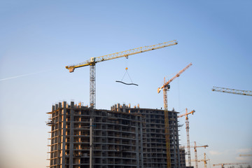 Tower cranes constructing a new residential building at a construction site against blue sky. Renovation program, development, concept of the buildings industry.