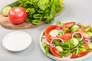 Healthy vegetarian dish on table, vegetable salad with fresh tomato, cucumber, lettuce, red onion on gray concrete background. Diet menu. mockup, template