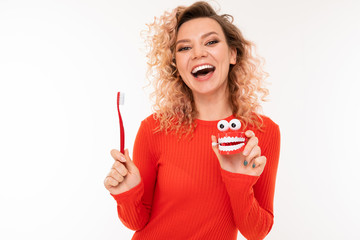 attractive curly European girl in a red dress holds a toothbrush in her hands on a white background