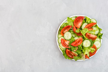Healthy vegetarian dish on table, vegetable salad with fresh tomato, cucumber, lettuce, red onion on gray concrete background. Diet menu. Top view. Flat lay, mockup, template with copy space