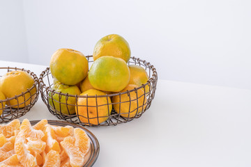 Beautiful peeled tangerines in a plate and metal basket isolated on bright white clean table in a modern contemporary kitchen island, close up.