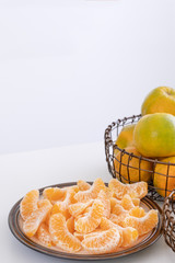 Beautiful peeled tangerines in a plate and metal basket isolated on bright white clean table in a modern contemporary kitchen island, close up.