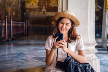 Smiling traveler Asian woman in a white a dress and straw hat, watching her mobile for find location