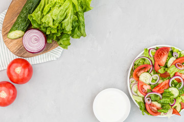 Healthy vegetarian dish on table, vegetable salad with fresh tomato, cucumber, lettuce, red onion on gray concrete background. Diet menu. Top view. Flat lay, mockup, template with copy space