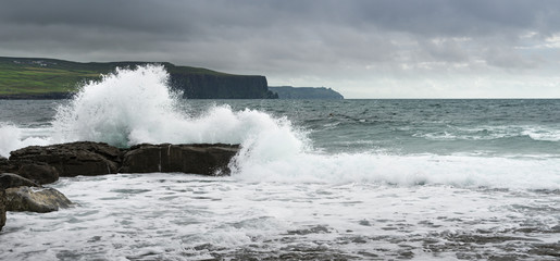 Panoramic view of the Irish coast in the Doolin area with cloudy sky and a wave in the foreground. © csbphoto