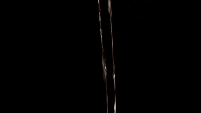 Water flowing from a tap. Abstract dark background with only a reflection of light showing movement.