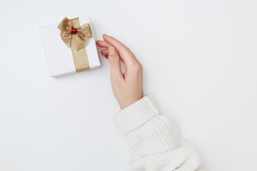 Women's hand holding present box with shiny golden ribbon and bow on the white background. Christmas concept