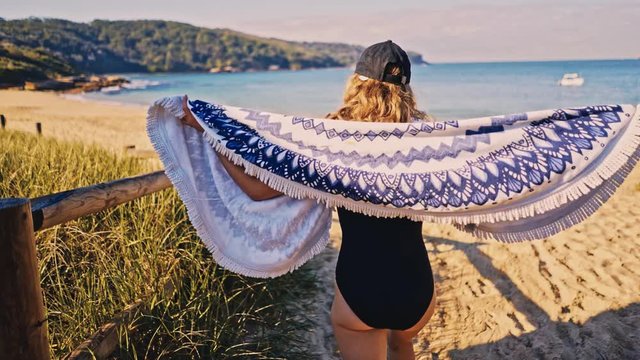 Young blond female wearing cap and pareo fabric at beach, Real time