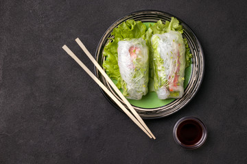 Fototapeta na wymiar Spring rolls with chopsticks on a green plate next to a gray sauce on a black background. There is a place for text