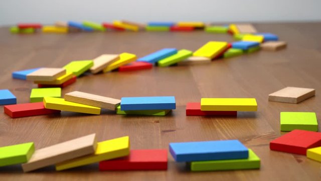 Dominoes of different colors falling on wooden background