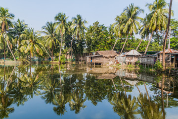 Fototapeta na wymiar Palms and village houses reflecting in a pond in Bagerhat, Bangladesh