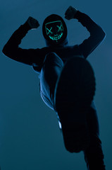 Anonymous man in black hoodie hiding his face behind a neon mask