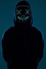 Anonymous man in black hoodie hiding his face behind a neon mask
