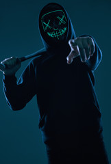 Anonymous criminal man with baseball bat in a black hoodie and neon mask