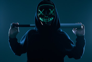 Anonymous criminal man with baseball bat in a black hoodie and neon mask - obrazy, fototapety, plakaty