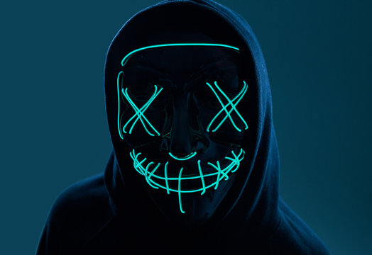 Anonymous man in black hoodie hiding his face behind a neon mask