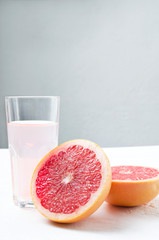 Vertical shot.Closeup of cutted grapefruit and glass of fresh squeezed juice on the white table against grey wall