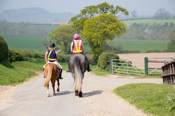 Rear view of two young women riding ponies out in the english countryside.