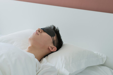 Fototapeta na wymiar asian young man sleeping in bed with an eye mask in bedroom