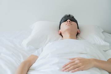 asian young man sleeping in bed with an eye mask in bedroom