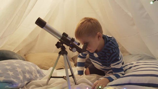 Little boy playing with a telescope in children's tent at home. Happy caucasian kid in the playroom.