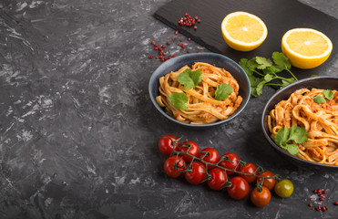 Semolina pasta with tomato pesto sauce, orange and herbs on a black concrete background. Side view, copy space.