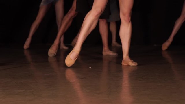 Close up of ballet dancer as she practices exercises on dark stage or studio. Woman's and mans feet in pointe shoes.