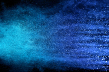 Abstract brown powder explosion. Closeup of blue dust particle splash isolated on black background.