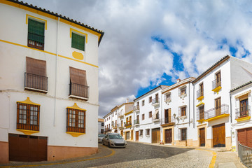 Fototapeta na wymiar A small narrow street with white houses and cars in the old European city. Ronda, Andalusia, Spain. Panorama