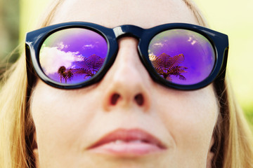 Woman wearing sunglasses with palms, sky reflection in mirror lens