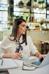 Attractive caucasian CEO sitting in cafe, holding cup of coffee and using laptop for work. Hardwork concept.