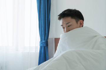 asian young man wrapped in plaid on bed