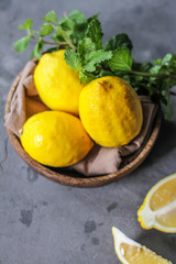 Photo of fresh ripe lemons on retro background. A slice of lemon with green leaves. Lemon fruit on wooden plate bowl. Top view. Copy space. Grey background. Image