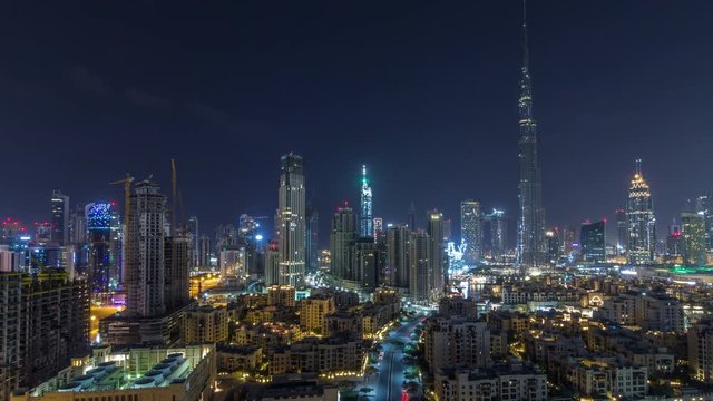 Dubai Downtown skyline during all night timelapse with Burj Khalifa and other towers paniramic view from the top in Dubai, United Arab Emirates. Moon on the sky. Traditional and modern buildings.