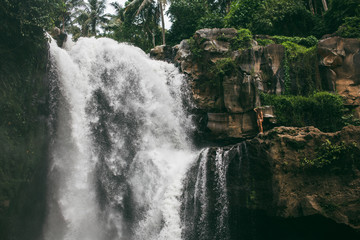 Beautiful girl posing in a swimsuit on the background of a large waterfall on the island of Bali. Tegenungan