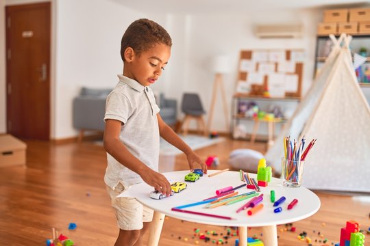 Beautiful african american toddler playing with cars around lots of toys at kindergarten